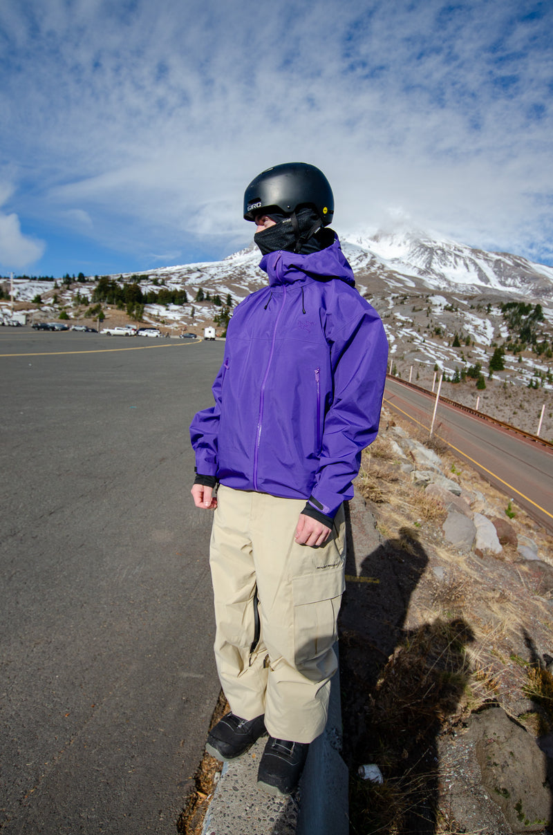 Person in a purple jacket and helmet standing on a road with a mountain in the background